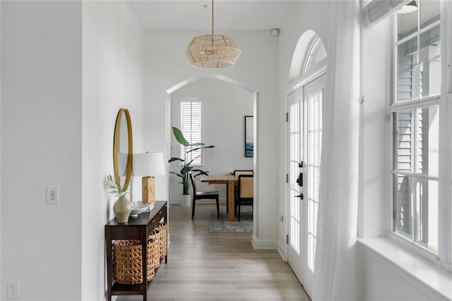 foyer with light wood-type flooring, a wealth of natural light, an inviting chandelier, and french doors