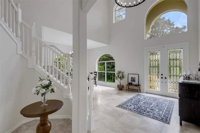 foyer with a high ceiling, a wealth of natural light, a notable chandelier, and french doors