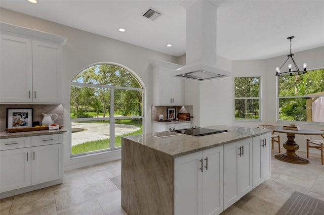 kitchen with light stone counters, a chandelier, black electric cooktop, island exhaust hood, and a kitchen island