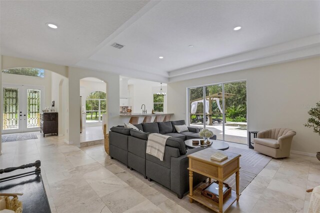 living room featuring french doors, a healthy amount of sunlight, a raised ceiling, and sink