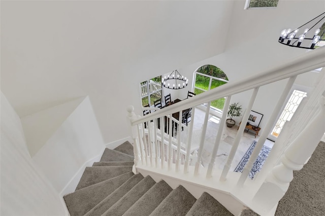 staircase featuring a towering ceiling, a chandelier, and carpet floors