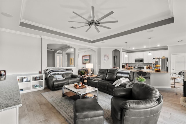 living room with a tray ceiling, ceiling fan, and light hardwood / wood-style floors