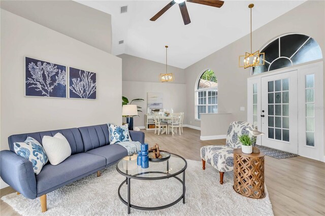 living room with ceiling fan with notable chandelier, light wood-type flooring, and vaulted ceiling