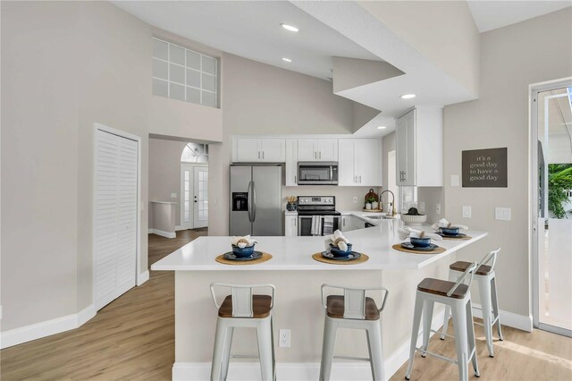 kitchen with high vaulted ceiling, stainless steel appliances, kitchen peninsula, sink, and white cabinets