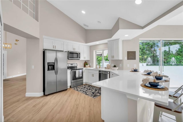 kitchen with appliances with stainless steel finishes, white cabinetry, light hardwood / wood-style flooring, and kitchen peninsula