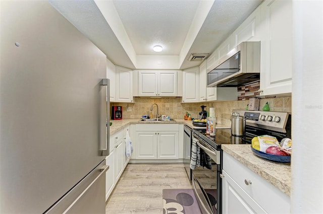 kitchen with sink, tasteful backsplash, light hardwood / wood-style flooring, appliances with stainless steel finishes, and white cabinets