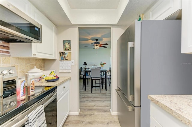 kitchen featuring white cabinets, backsplash, ceiling fan, light hardwood / wood-style floors, and stainless steel appliances