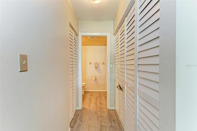 hallway with light hardwood / wood-style flooring and a textured ceiling