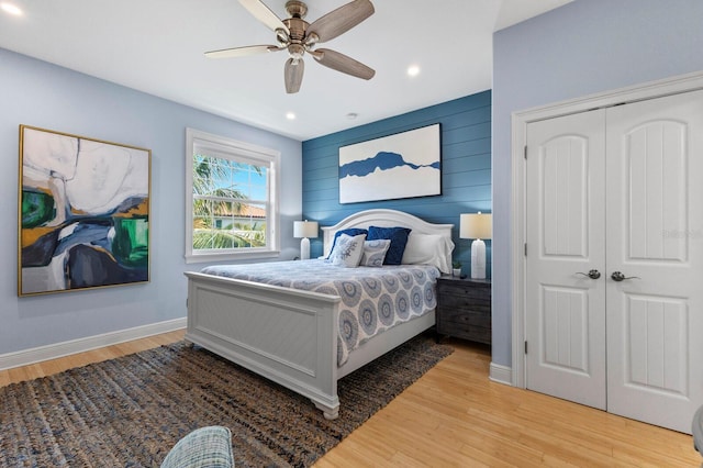 bedroom featuring light hardwood / wood-style floors, wood walls, ceiling fan, and a closet