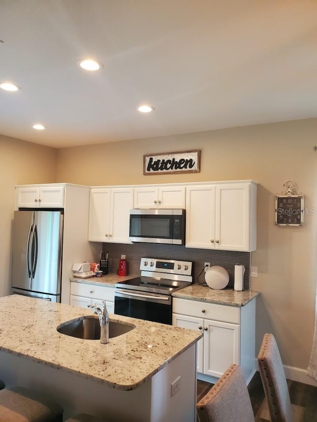 kitchen with appliances with stainless steel finishes, white cabinetry, a kitchen bar, and sink