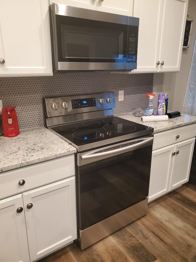 kitchen with backsplash, appliances with stainless steel finishes, light stone counters, white cabinetry, and dark wood-type flooring