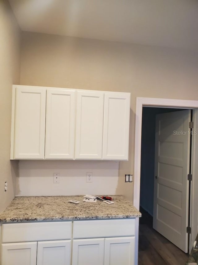 kitchen featuring dark hardwood / wood-style flooring, light stone countertops, and white cabinetry