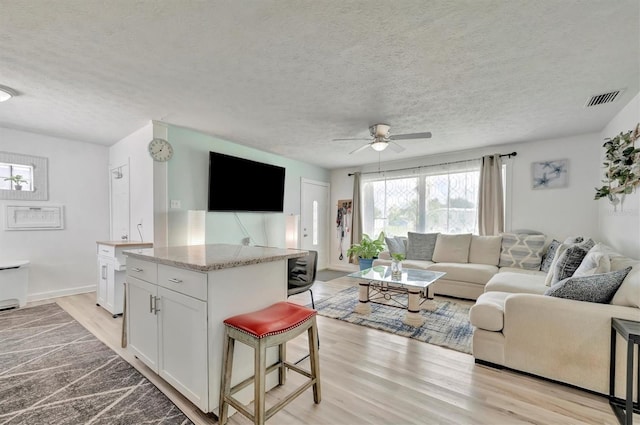 living room featuring a ceiling fan, baseboards, visible vents, light wood-style flooring, and a textured ceiling