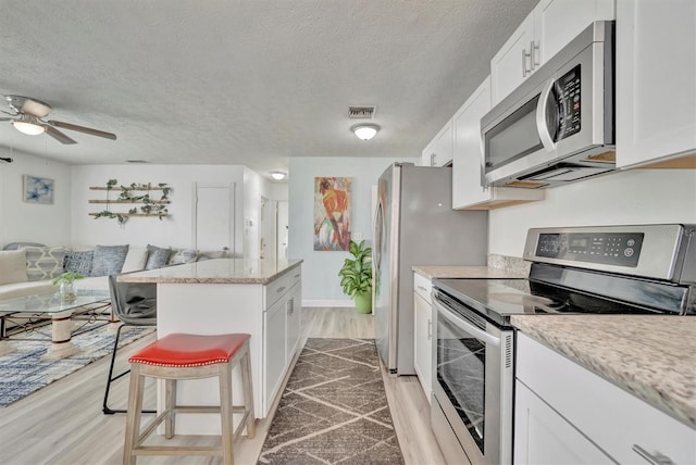 kitchen with white cabinets, light wood-type flooring, stainless steel appliances, ceiling fan, and a kitchen breakfast bar