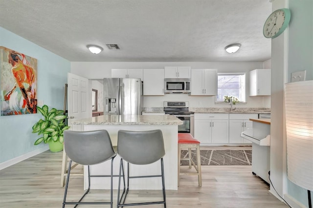 kitchen with a textured ceiling, a center island, appliances with stainless steel finishes, white cabinets, and light hardwood / wood-style floors