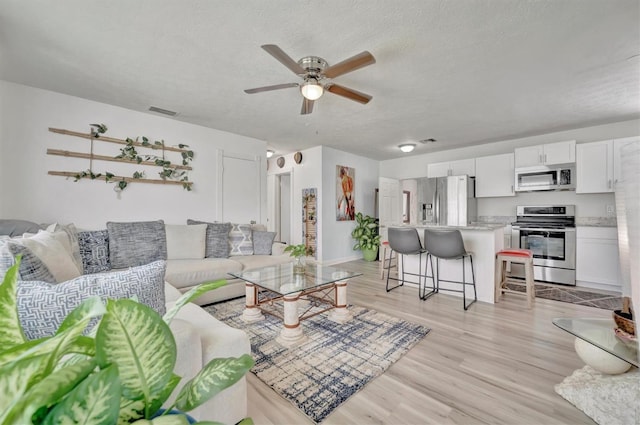 living area featuring visible vents, light wood-style flooring, a textured ceiling, and a ceiling fan