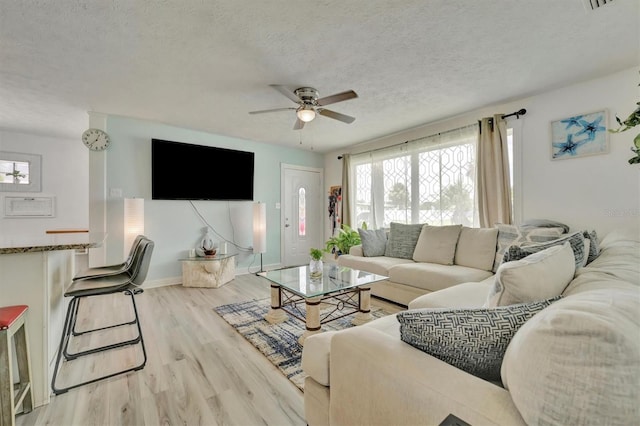 living room with light wood-type flooring, ceiling fan, and a textured ceiling