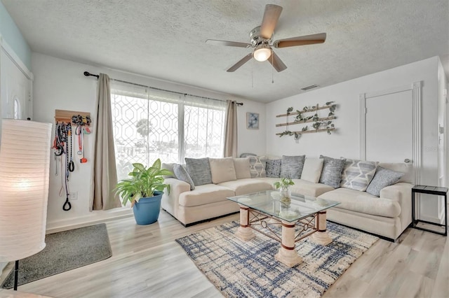 living room with ceiling fan, a textured ceiling, and light hardwood / wood-style flooring