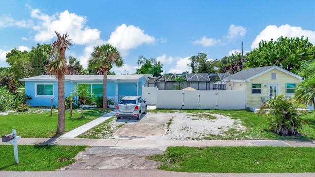 view of front of home with a front yard, a gate, fence, driveway, and a lanai