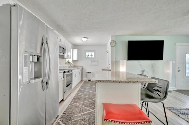 kitchen with light wood-type flooring, appliances with stainless steel finishes, white cabinetry, and a textured ceiling