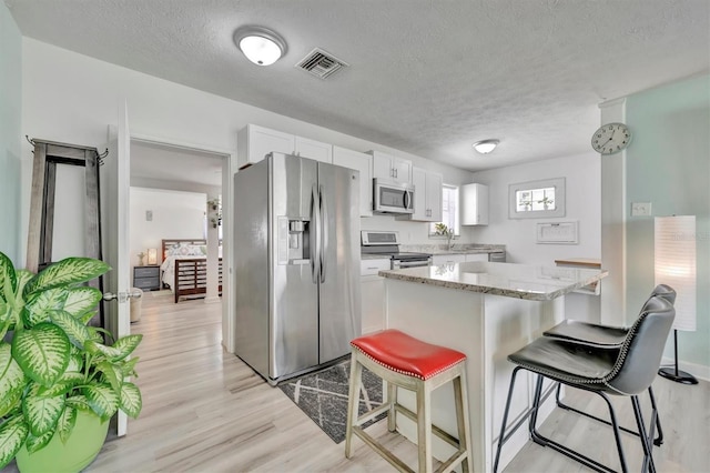 kitchen with visible vents, a breakfast bar, stainless steel appliances, white cabinets, and light wood-type flooring