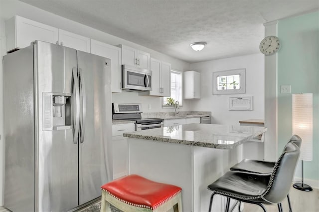 kitchen with a textured ceiling, a kitchen breakfast bar, appliances with stainless steel finishes, light stone counters, and white cabinets