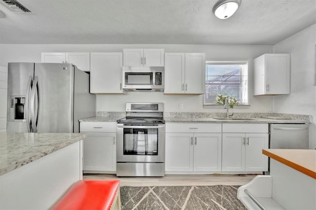 kitchen with white cabinets, stainless steel appliances, a textured ceiling, and light hardwood / wood-style flooring