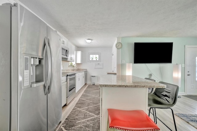 kitchen featuring a breakfast bar area, a sink, appliances with stainless steel finishes, white cabinetry, and a center island