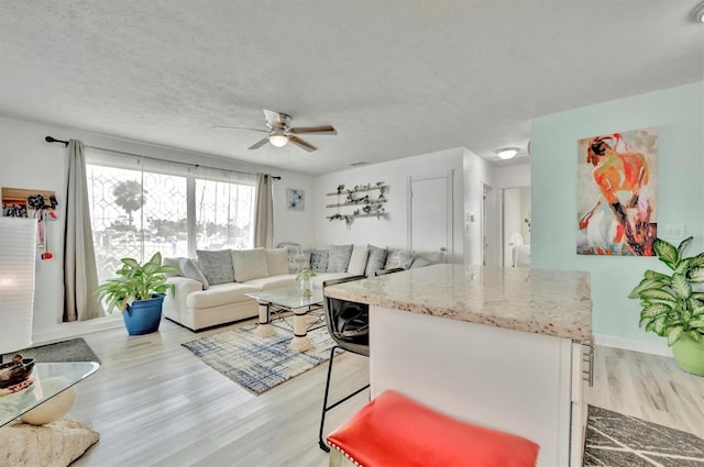 kitchen with white cabinets, light hardwood / wood-style floors, a breakfast bar area, ceiling fan, and a textured ceiling