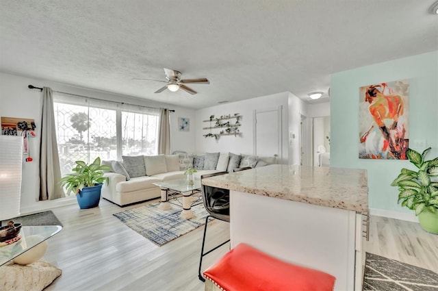 living area with a textured ceiling, light wood-style flooring, and ceiling fan