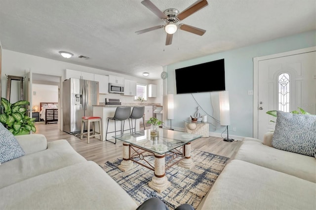 living room featuring ceiling fan, light hardwood / wood-style floors, and a textured ceiling