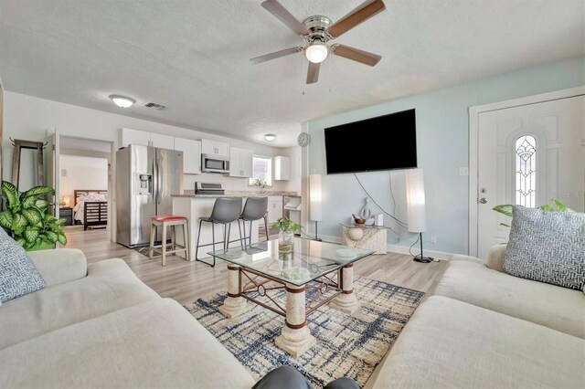 living room featuring a ceiling fan, baseboards, visible vents, light wood-style flooring, and a textured ceiling