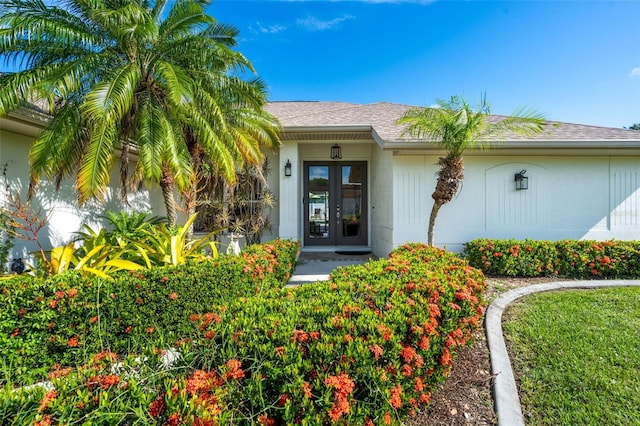 doorway to property featuring a shingled roof, french doors, and stucco siding