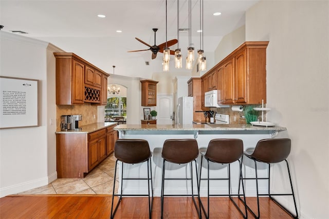 kitchen with a peninsula, a kitchen breakfast bar, brown cabinets, and white appliances