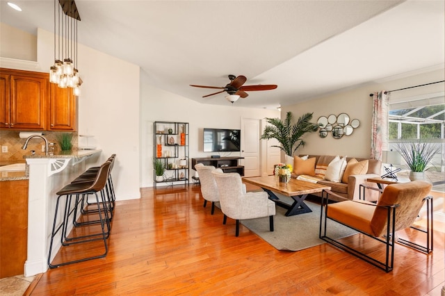 living room with ceiling fan with notable chandelier, lofted ceiling, light hardwood / wood-style flooring, and sink