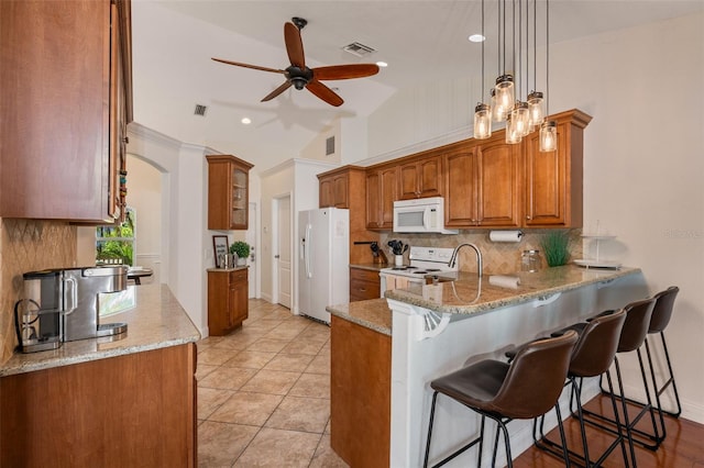 kitchen featuring ceiling fan with notable chandelier, white appliances, pendant lighting, and light stone countertops