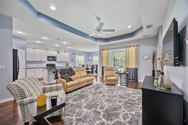 living room with a textured ceiling, dark wood-type flooring, ceiling fan, and a tray ceiling