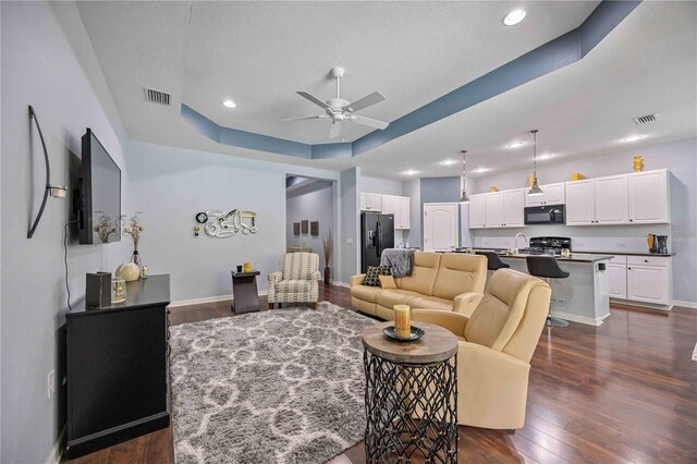 living room featuring a textured ceiling, dark wood-type flooring, ceiling fan, and a tray ceiling