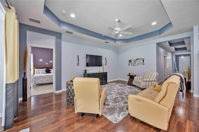 living room featuring a raised ceiling, dark hardwood / wood-style flooring, ceiling fan, and a textured ceiling