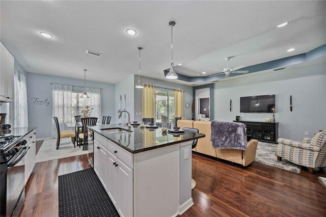 kitchen with white cabinetry, an island with sink, sink, ceiling fan, and dark wood-type flooring