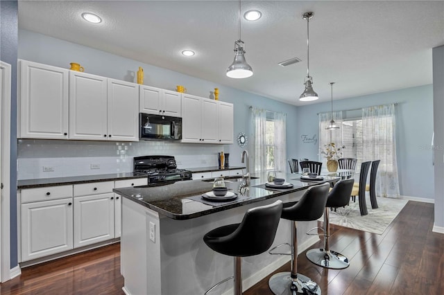 kitchen featuring decorative light fixtures, black appliances, dark hardwood / wood-style floors, and a center island with sink