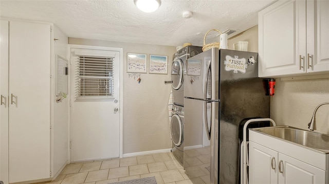 interior space with sink, stainless steel fridge, white cabinets, stacked washer and clothes dryer, and a textured ceiling