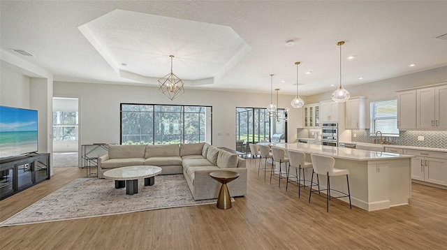 living room featuring a raised ceiling, an inviting chandelier, a textured ceiling, and light hardwood / wood-style flooring