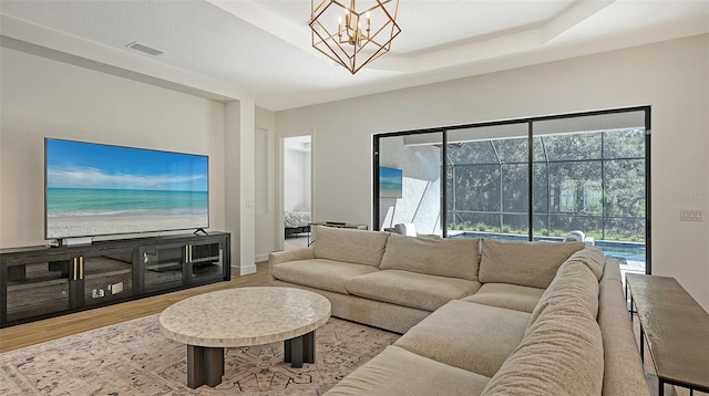 living room with a raised ceiling, a chandelier, and light hardwood / wood-style floors