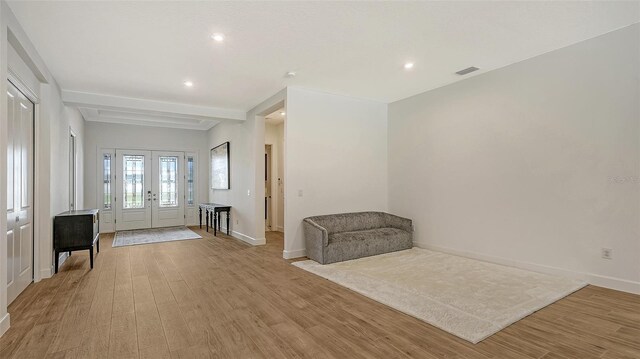 unfurnished living room featuring light hardwood / wood-style flooring, beamed ceiling, and french doors