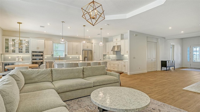 living room with plenty of natural light, an inviting chandelier, sink, and light hardwood / wood-style floors