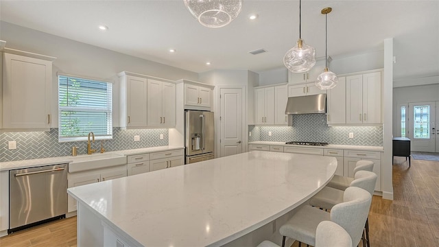 kitchen with hanging light fixtures, stainless steel appliances, white cabinetry, and light hardwood / wood-style floors