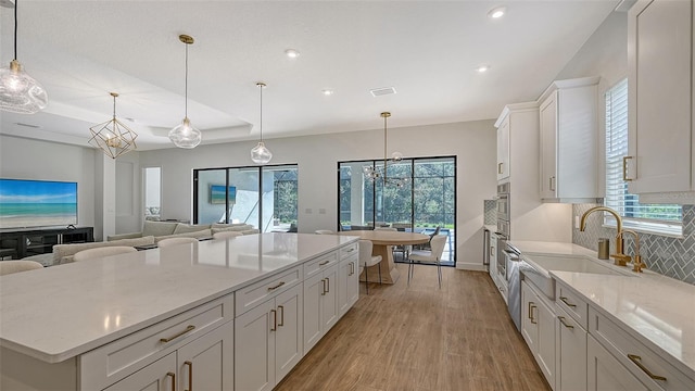 kitchen with light wood-type flooring, backsplash, a center island, hanging light fixtures, and white cabinets