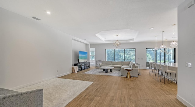 living room featuring a tray ceiling, a chandelier, and light hardwood / wood-style floors