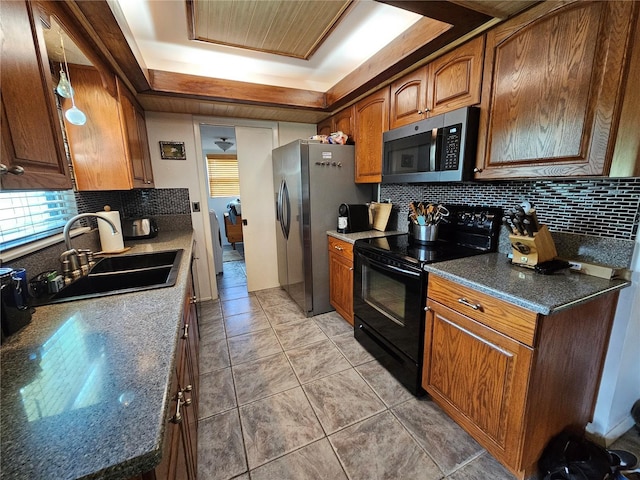 kitchen with backsplash, light tile patterned floors, appliances with stainless steel finishes, brown cabinetry, and a sink